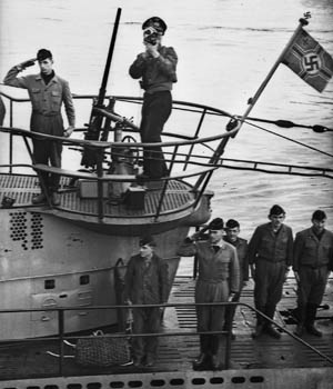 While U-99 returns to its base at Lorient on the coast of France, two crewmen render military salutes while others stand at attention on deck. Another sailor is preoccupied with capturing the U-boat’s return on film.