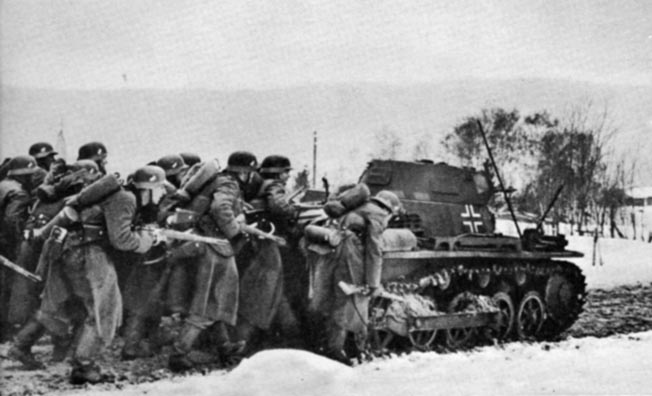 Crouching behind a Panzer I, German infantrymen advance during an assault on a Norweigan village, April 1940.
